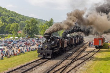 a steam train on a track with smoke coming out of it with Cass Scenic Railroad State Park in the background